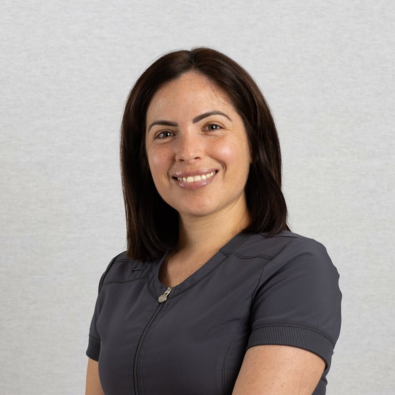 Medical headshot of a smiling clinical staff member in grey scrubs