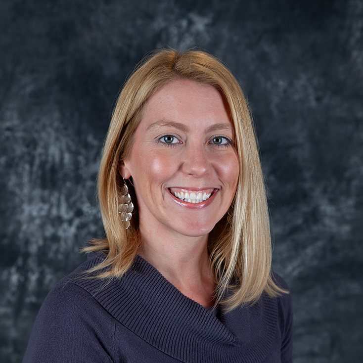 Professional headshot of a smiling blonde woman in a purple sweater