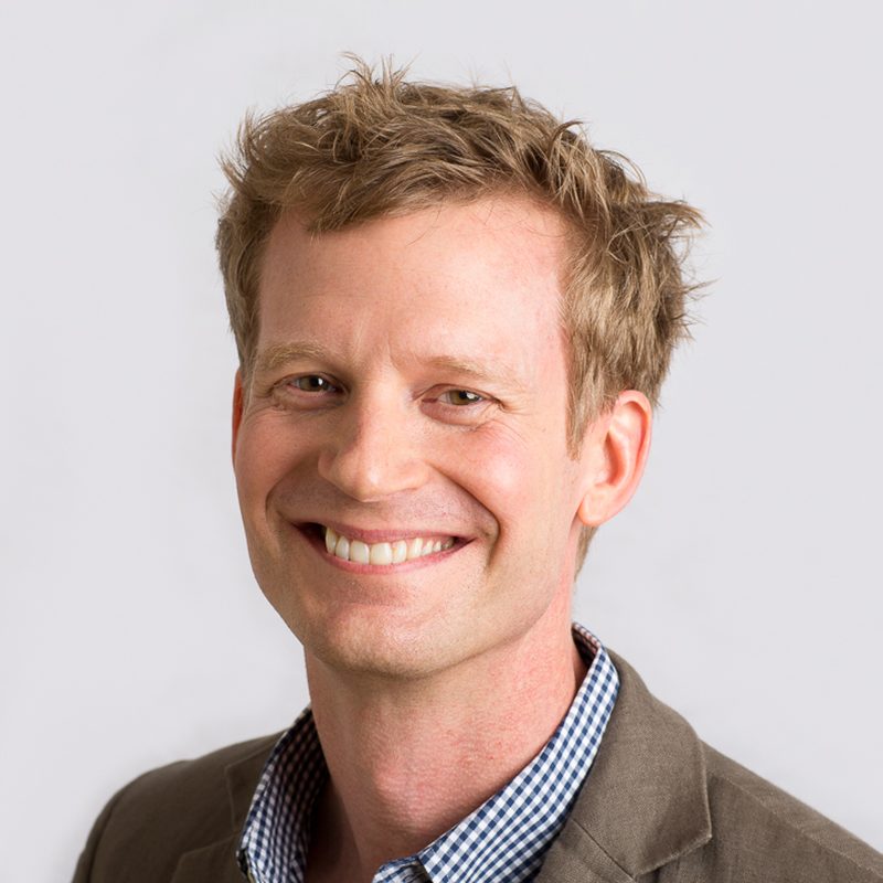 Real estate agent headshot of a smiling man in a checked shirt and tan jacket